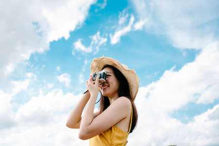 Beautiful asian traveler woman taking photo with vintage film camera on bright sky background.