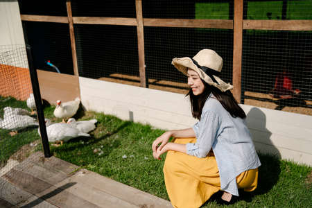 Beautiful asian farmer woman wear hat looking at duck herd outdoors.