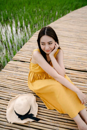 Beautiful asian traveler woman sitting on wooden bridge in rice field.の写真素材