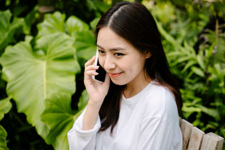 Beautiful asian woman in white shirt talking on the phone at park outdoors.の写真素材