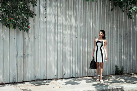 Asian woman stading in the shadow of trees carrying black bag.の写真素材