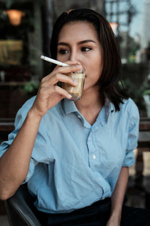 Thai woman drinking coffee while holding cigarette with right hand.の写真素材