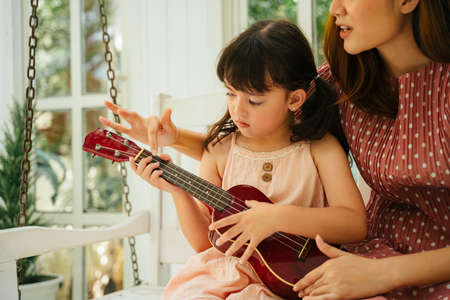 Asian mother and daughter practice ukulele together at home backyard.の写真素材