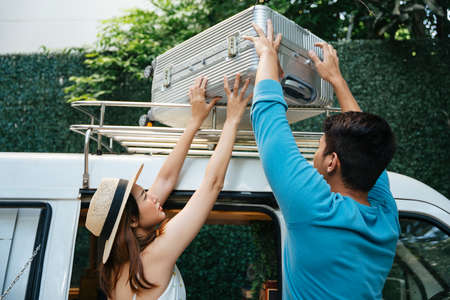 Asian couple packing luggages and bags on car roof for roadtrip.
