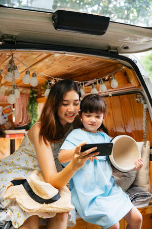 Asian mother and child having fun taking selfie with smartphone at RV car trunk.の写真素材