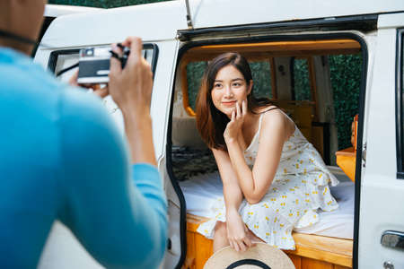 Asian couple taking photo inside recreational vehicle, standing beside a car.の写真素材