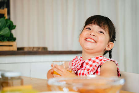 Big smile asian little girl enjoy drinking water in kitchen.
