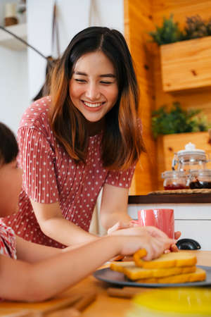 Asian mother prepare bread toast for breakfast to her child at home.の写真素材