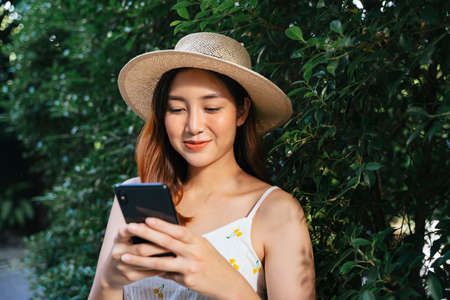 Cheerful asian woman wear hat chatting on smartphone at park.の写真素材