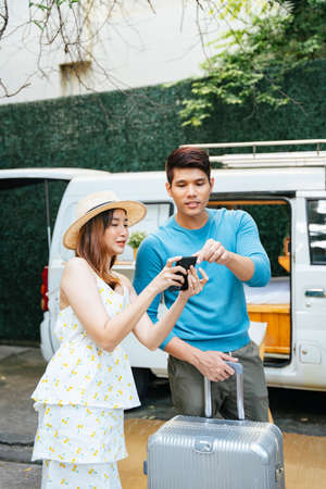 Asian couple looking at digital map on smartphone before roadtrip.