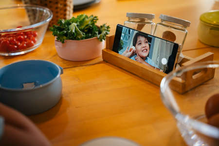 Child doing cooking vlog with smartphone at kitchen table.