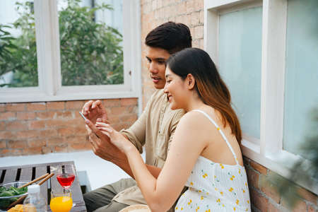 Asian couple ordering food from digital menu on smartphone at restaurant.