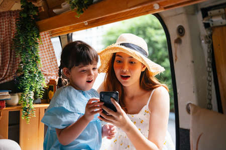Asian mother and child looking at screenshot on smartphone inside recreational vehicle.