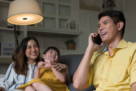 Asian family spending time together at home. Father talking on the phone. Mother and daughter looking at father.の写真素材