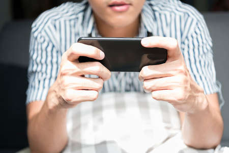 Close up hand of asian man playing mobile game at home.