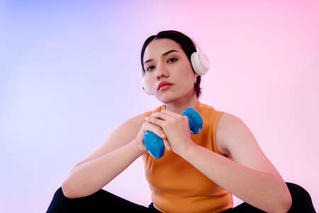 Portrait of asian healthy woman wear headphone and work out with dumbbell.