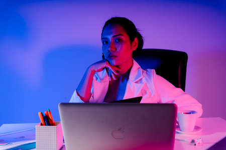 Modern asian businesswoman working at office desk. Colored neon light tones.
