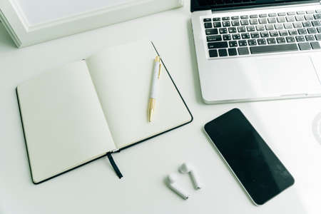 Top view - Minimal working desk in office with blank book, smartphone, laptop, and earphones.の写真素材