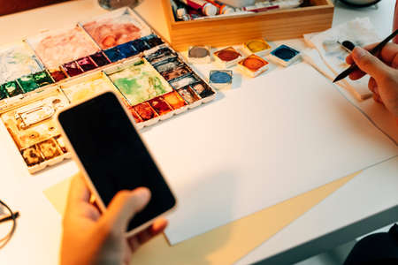 Top view - Water colour artist working desk with mock up paper and smartphone for finding reference.の写真素材