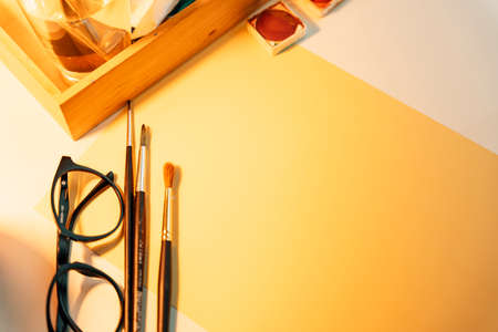 Top view - Working desk for artist with eyeglasses, brushes, and colour palette.の写真素材