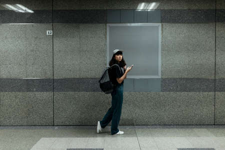 Sideview of Asian thai backpacker woman traveler wearing cap walking in metro underground infront of...