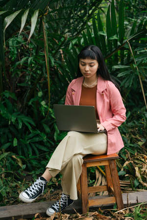 Asian business woman in formal shirt sitting on a chair using computer laptop in nature.