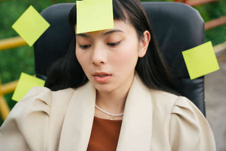 Asian business woman in formal shirt sitting on a chair with many sticky notes paper around her.