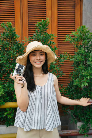 Fashion portrait of young asian woman with vintage camera. Beautiful photographer at resort.