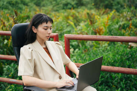 Asian business woman in formal shirt sitting on a chair using computer laptop on a bridge outdoors.の写真素材