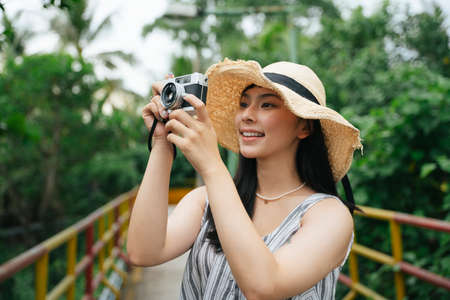 Fashion portrait of young asian woman with vintage camera. Beautiful photographer at resort.
