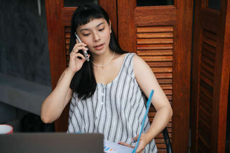 Asian business woman working at home talking on the phone.