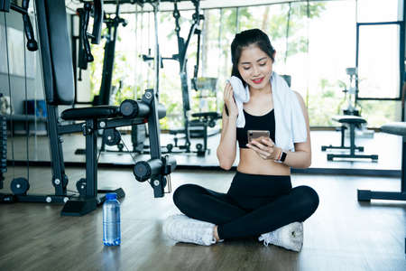 Healthy asian woman take a break after work out in gym, using smartphone.