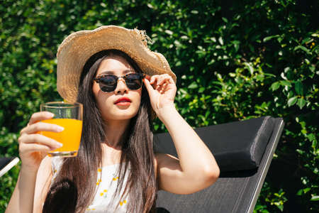 Portrait of asian traveler woman wear sunglasses and hat enjoy orange juice in summer.