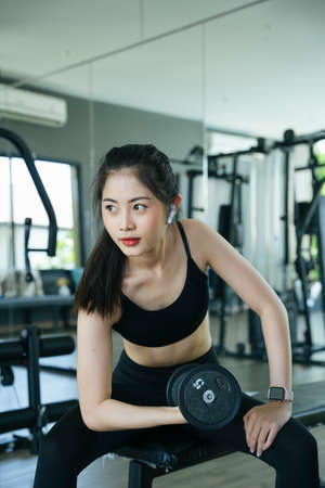 Healthy asian woman exercise with dumbbell and listen to music in gym.の写真素材