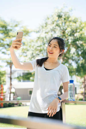 Sporty asian woman vlogging about exercise or selfie with smartphone at park.の写真素材