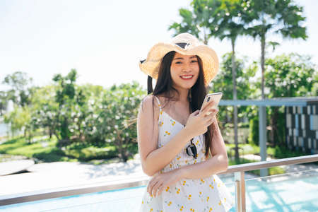 Beautiful asian traveler woman wear hat using smartphone at hotel balcony.