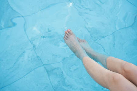 Legs of woman enjoy playing water at swimming pool.