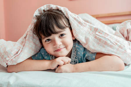 Cheerful girl having fun under blanket in bedroom.