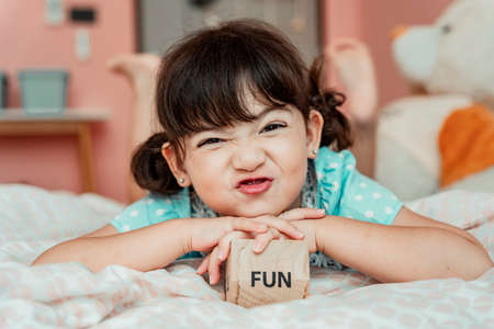 Portrait of little girl laying on bed with toy wooden block. Fun stuff concept.の写真素材