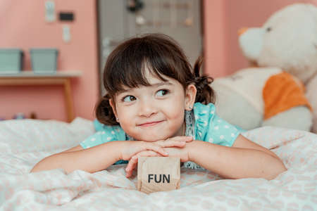 Portrait of little girl laying on bed with toy wooden block. Fun stuff concept.の写真素材