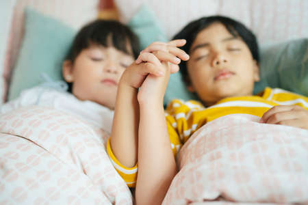 Sister and brother holding hands while sleeping on the bed. Selective focus.の写真素材
