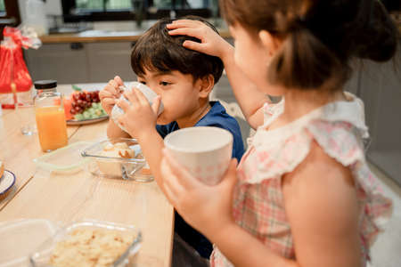 Lovely brother and sister taking care of each other in kitchen while eating food together.の写真素材