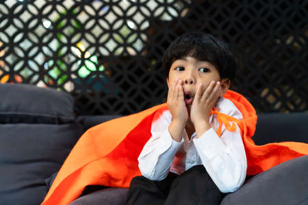 Asian boy dress up with orange hood sitting on sofa in halloween party.の写真素材