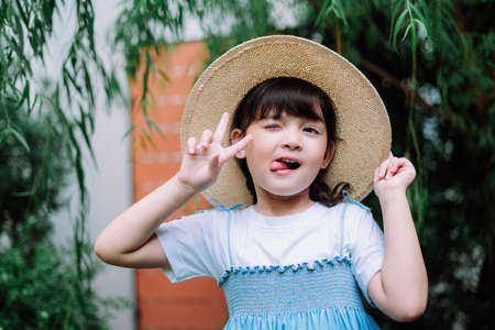 Portrait of adorable girl in white blue dress wearing straw hat with victory gesture.の写真素材