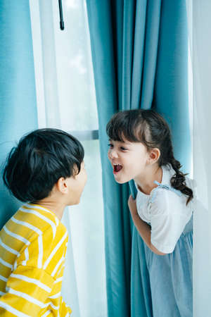 Playful boy and girl having fun playing and looking at each other face behind the curtain.の写真素材