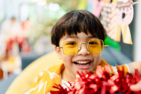 Portrait of little boy playing with red tinsel on a couch at home.の写真素材