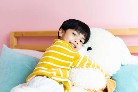 Asian little boy hugging fluffy big bear doll in bedroom.の写真素材