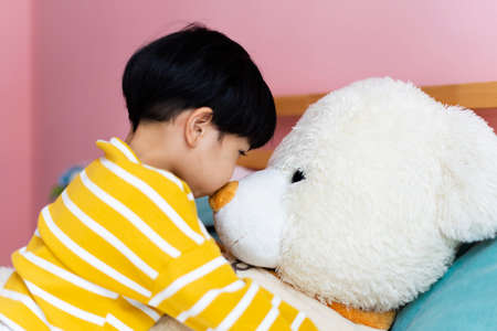 Asian little boy hugging fluffy big bear doll in bedroom.の写真素材