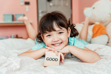 Portrait of little girl laying on bed with toy wooden block. Good stuff concept.の写真素材