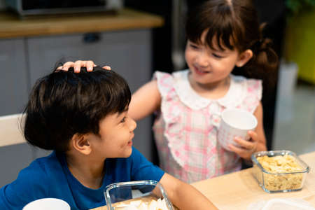 Big sister pating her brother head while having dinner at home.の写真素材